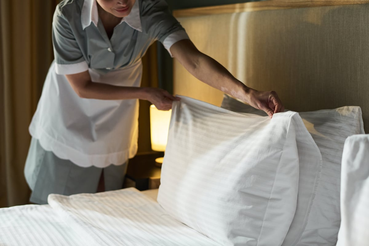 Housekeeper smoothing sheets and arranging pillows on a freshly made bed